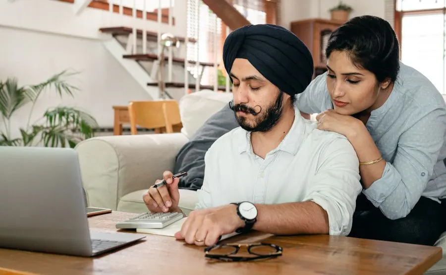 A couple working out numbers together at home with a calculator and laptop